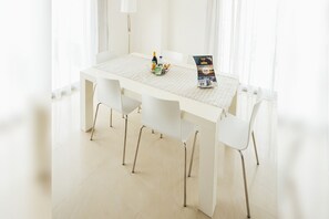 A white dining table with six chairs, a magazine, and a bottle on it.