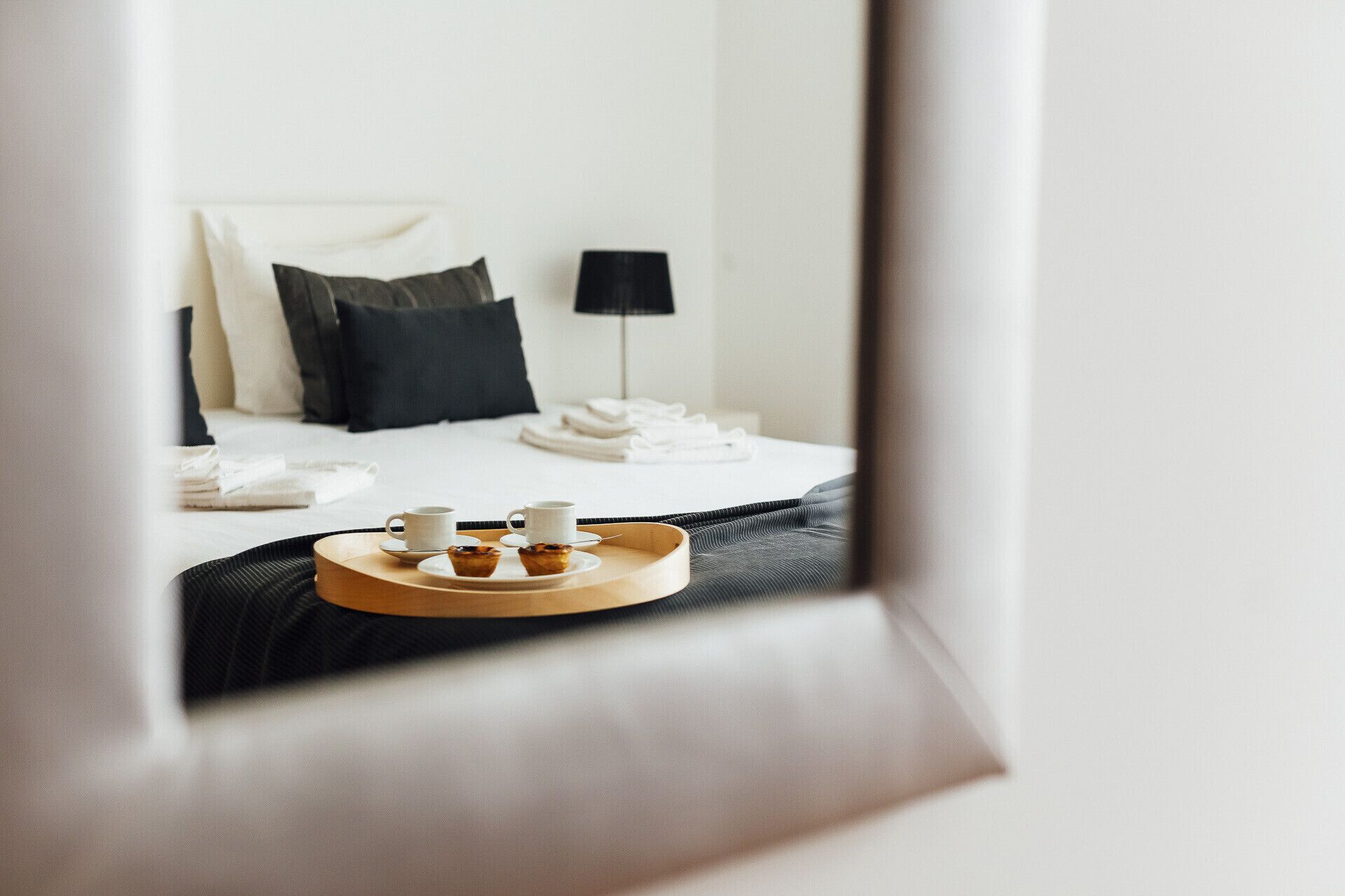 Une chambre d’hôtel avec un lit bien fait, une table de chevet avec une lampe et un plateau avec deux tasses et deux viennoiseries.