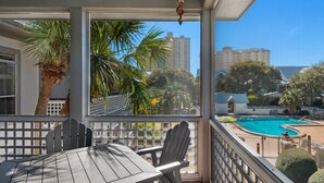 A balcony with a table and chairs, overlooking a swimming pool and palm trees. - Wrap-Around Balcony, Two Swimming Pools, Walk to the Beach (Miramar Beach)