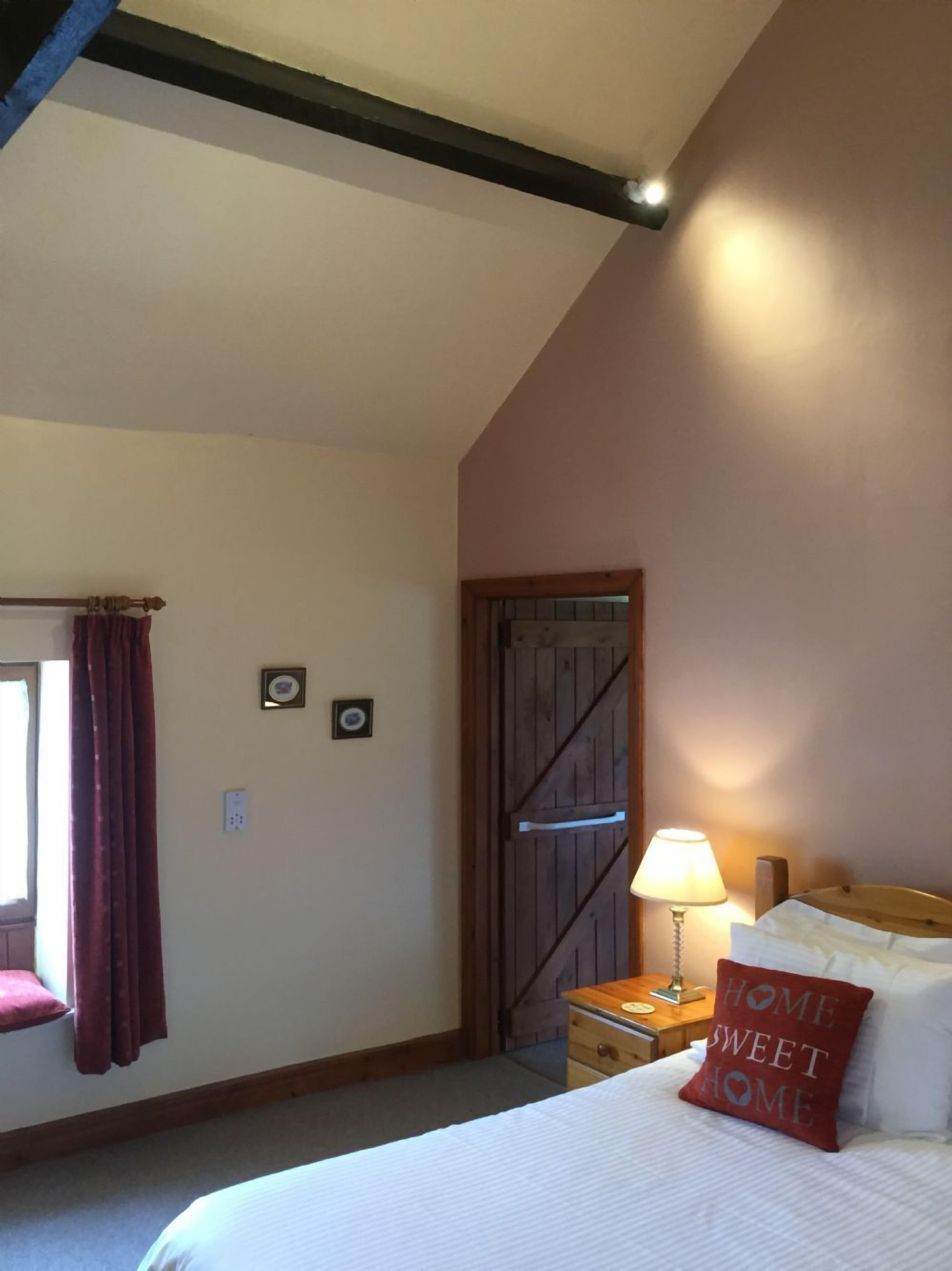 A bedroom with a bed, a nightstand, a lamp, a wooden door, and a window with curtains.