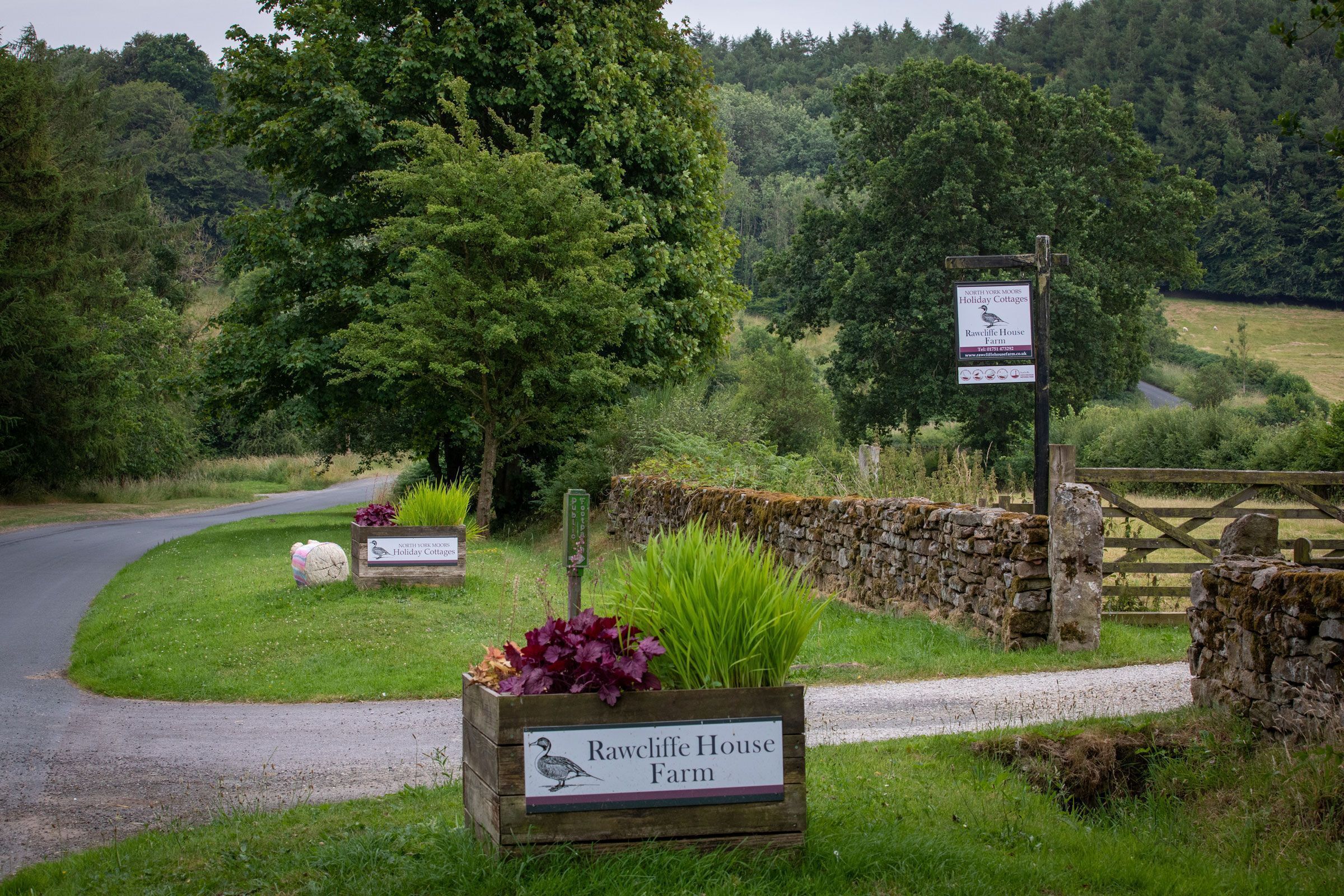 A rural setting with a sign for Rawcliffe House Farm, surrounded by greenery and stone walls.
