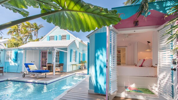 Ett poolområde med en solstol, en liten pool och en byggnad med en rosa och blå fasad.