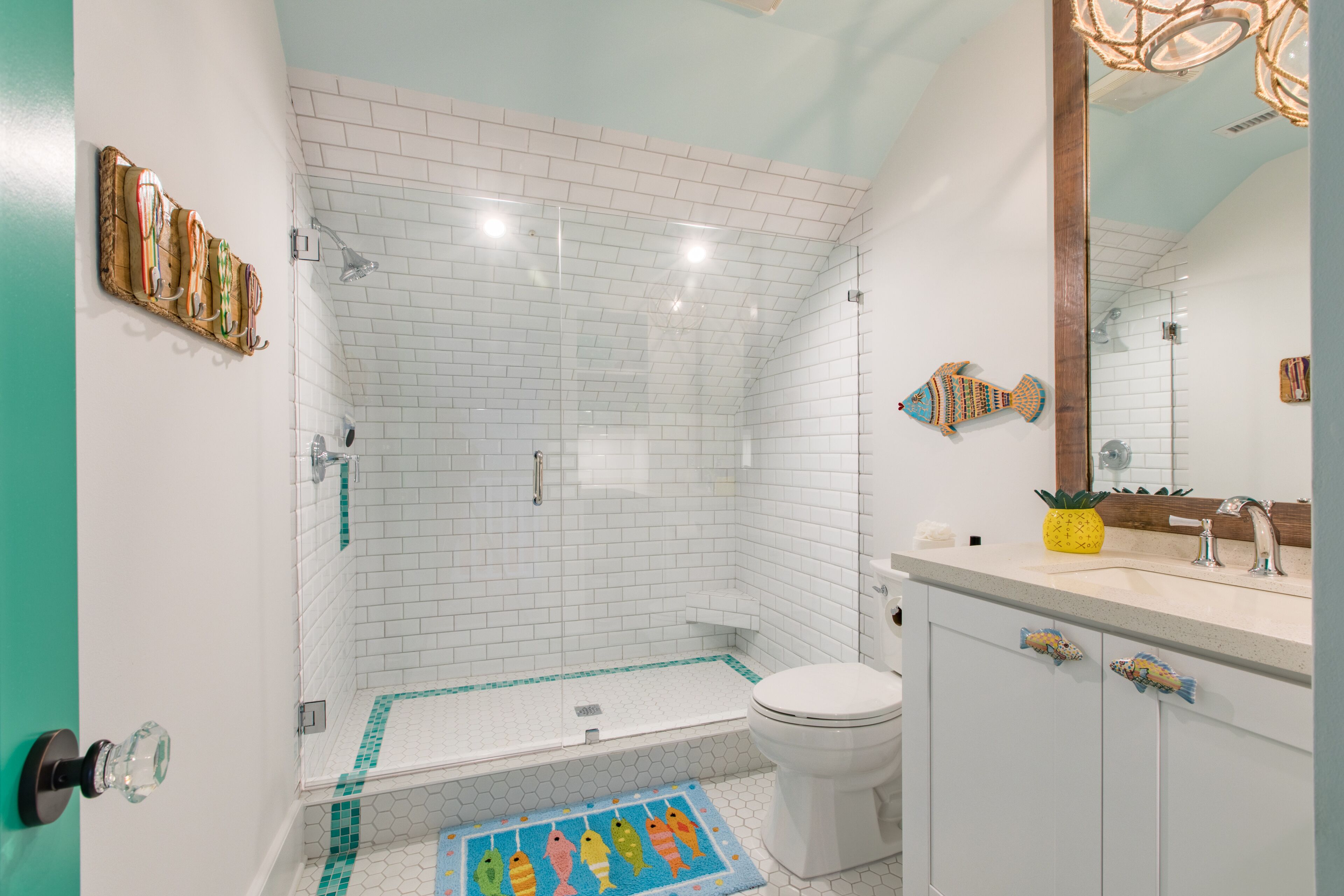 Ein Badezimmer mit weißen Fliesen im U-Bahn-Stil, einer Glasdusche, einer Toilette, einem Waschbecken mit Spiegel und dekorativen Fischbildern an der Wand.