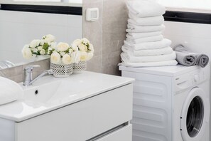 Une salle de bain moderne avec un lavabo blanc, un vase de fleurs blanches et une pile de serviettes blanches.