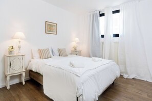 Une chambre à coucher avec un lit, deux tables de chevet avec des lampes, un tableau encadré au mur et une fenêtre avec des rideaux.