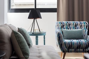 A living room with a sofa, a patterned armchair, a small table, and a floor lamp.