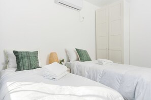A hotel room with two beds, white bedding, and a large wardrobe.