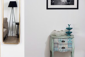 A room with a mirror, a small table with decorative items, and a framed picture on the wall.