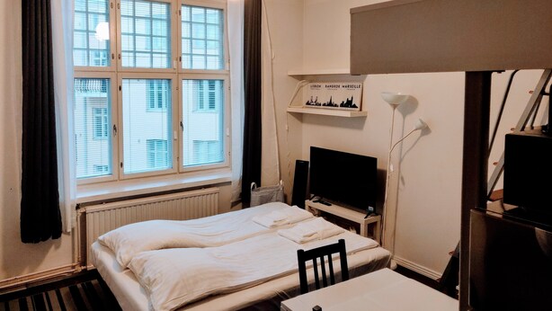 Habitación de hotel con cama, escritorio, silla, televisor y ventana con cortinas.