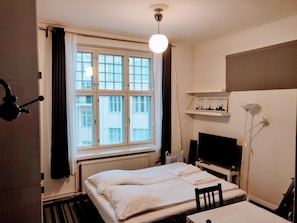 Een hotelkamer met een bed, een bureau, een televisie, een boekenkast met reisgidsen en een raam met gordijnen.
