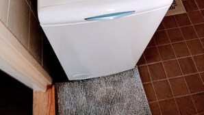 Una lavadora blanca en un baño con paredes de azulejos y piso marrón.