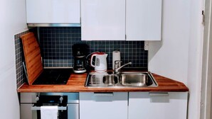 Una cocina compacta con armarios blancos, una encimera de madera, una cafetera, un hervidor y un lavamanos de acero inoxidable.