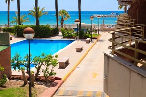 A pool area with a view of the ocean, benches, and a pathway leading to the beach. - Beachfront Apartment with Pool · UHC SOL DE ESPAÑA 208 (Cambrils)