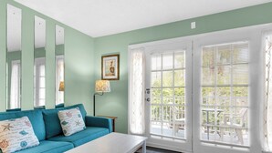 A room with teal walls, a white sofa with decorative pillows, a white coffee table, and a large window with blinds. - At the Beach - Gulf Views - Pool (Miramar Beach)