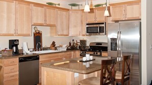 A modern kitchen with wooden cabinets, stainless steel appliances, a central island, and pendant lighting. - Promo! Oceanfront Condo w/ Private Hot Tub, Indoor Pool, WiFi and More! (Lincoln City)
