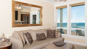 A living room with a beige sofa, patterned cushions, a round coffee table, a large mirror, and a view of the beach through large windows. - Promo! Oceanfront Condo w/ Private Hot Tub, Indoor Pool, WiFi and More! (Lincoln City)