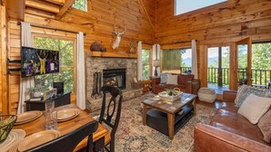 A wooden cabin interior with a stone fireplace, a television, a dining table, and a cozy seating area. - AMAZING VIEWS! Firepit, Private, Woodburning Fireplace, Hot Tub, Pool Table! (Sevierville)
