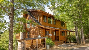 A wooden cabin with a porch, a covered deck, and a log storage area. - AMAZING VIEWS! Firepit, Private, Woodburning Fireplace, Hot Tub, Pool Table! (Sevierville)