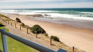 A beach with a clear view of the ocean, a sandy shore, and a grassy area with a fence. - Promo! Second Floor Corner Condo, Oceanfront, Private Hot Tub, Pool, Wifi (Lincoln City)