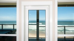 A view from a balcony overlooking the ocean with a door in the foreground. - Promo! Second Floor Corner Condo, Oceanfront, Private Hot Tub, Pool, Wifi (Lincoln City)