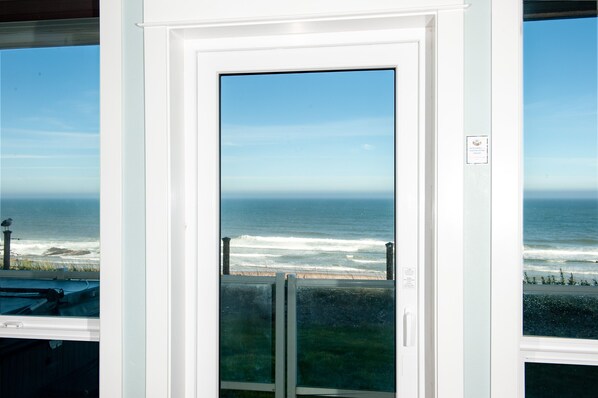 Vista a través de una puerta que da al océano y a la playa, con cielo despejado y un cartel en la pared.