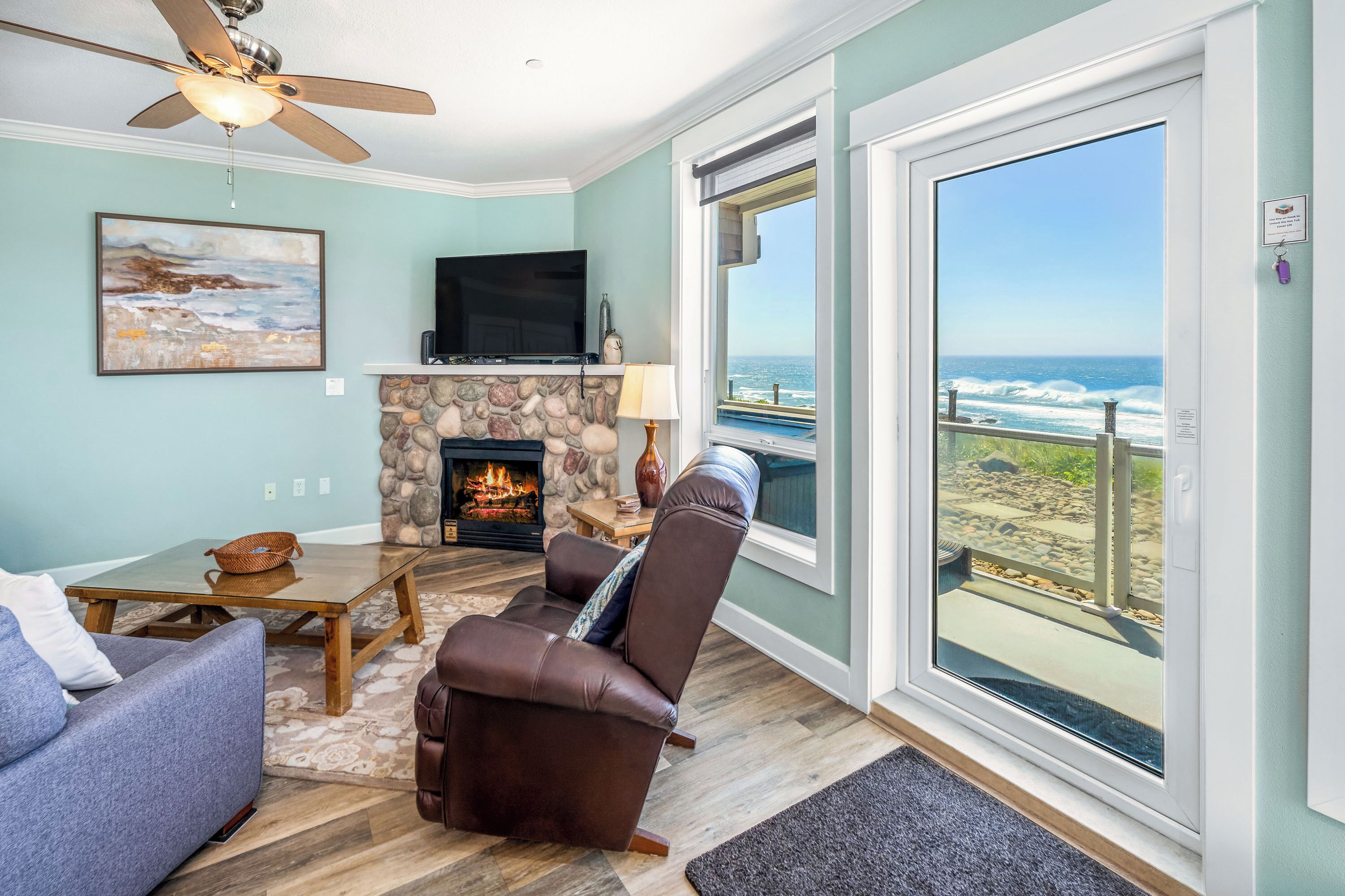 A living room with a stone fireplace, a television, and a view of the ocean.