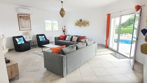 Een moderne woonkamer met een grijze bank, zwarte fauteuils en een salontafel. Er is een groot raam met uitzicht op groen.