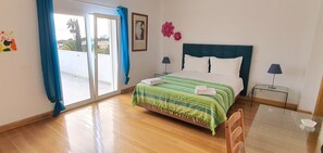 Ein Schlafzimmer mit Bett, Nachttisch, Stuhl, Tisch, einem Fenster mit Vorhängen und Blick nach draußen.