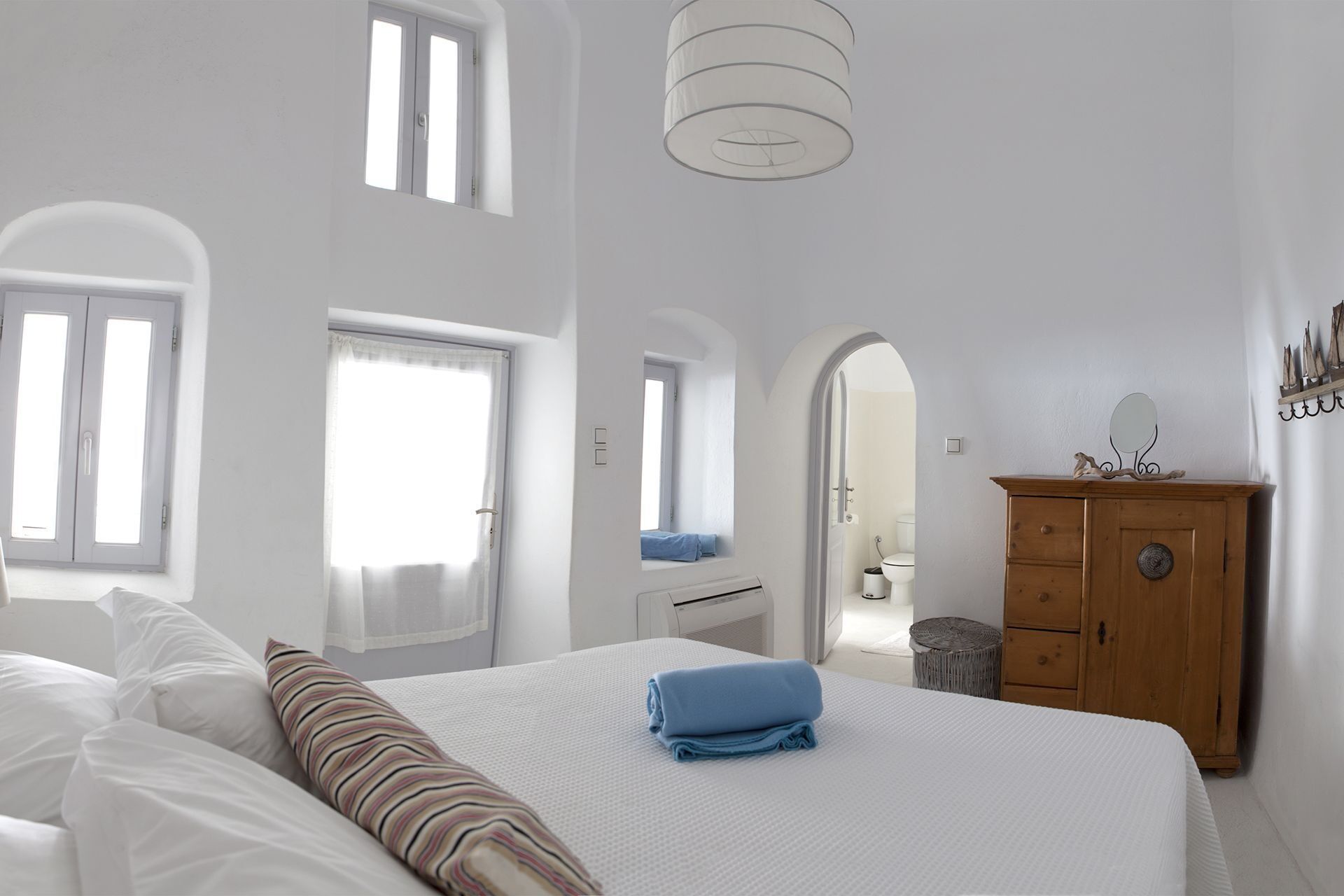 A bedroom with a bed, a wooden dresser, a mirror, and a window.