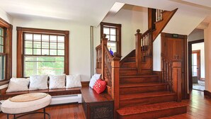 A spacious living room with a wooden staircase, large windows, and a cozy seating area.