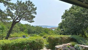 A garden with a variety of plants and a large tree. There is a view of the ocean and a distant lighthouse.