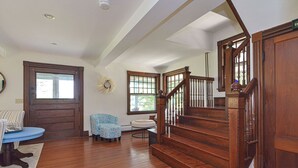 A spacious living room with hardwood floors, a blue armchair, a round coffee table, and a staircase with wooden railings.