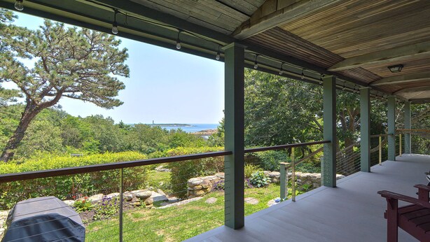 A covered outdoor area with a view of the sea, featuring a wooden deck, metal railings, and a stone pathway.