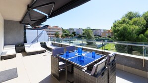 A balcony with a table and chairs, a sofa, and a glass railing overlooking a cityscape. - Penthouse with pool view - UHC SALOU VILLA FAMILY COMPLEX 029 (Salou)
