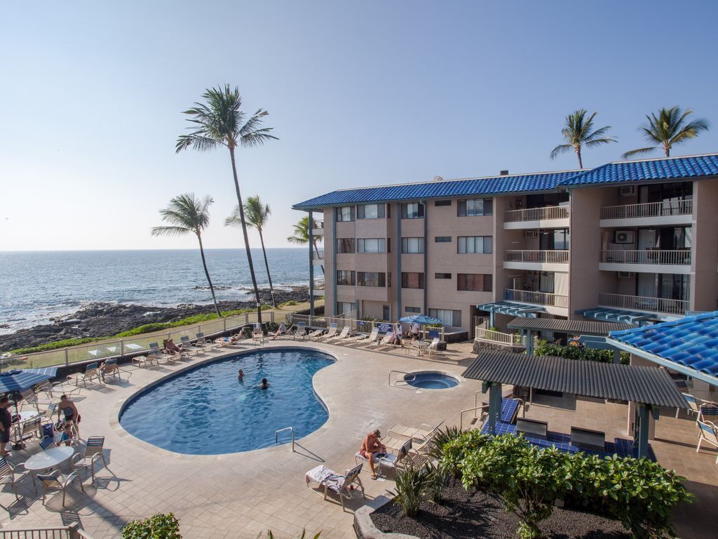 A hotel with a pool, palm trees, and a view of the ocean.