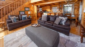 Interior acogedor de una cabaña de madera con sala de estar que incluye dos sofás, una mesa de centro y una escalera.