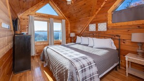 Un dormitorio acogedor tipo cabaña de madera, con cama, ventilador de techo, ventana y una mesita.