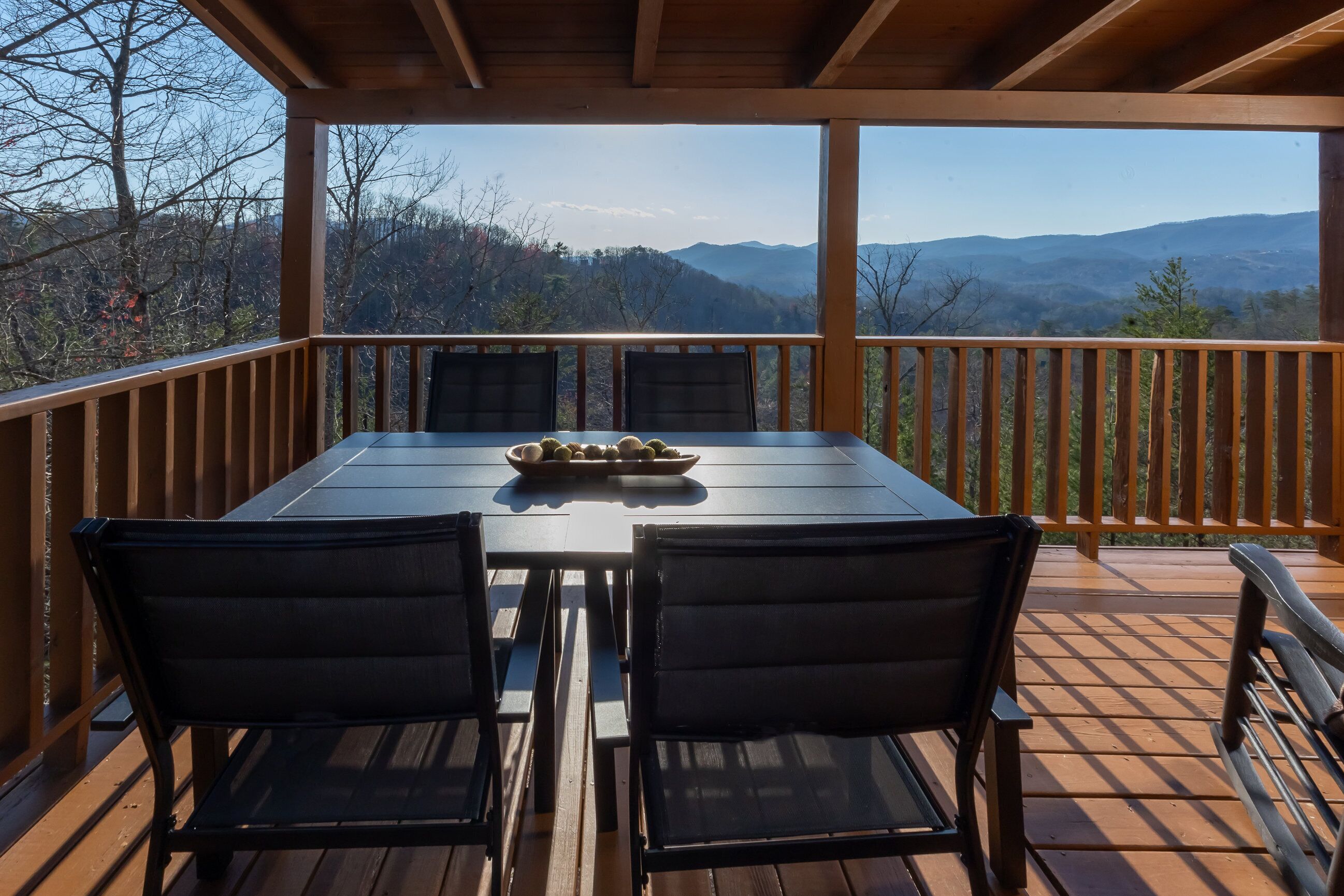 Una terraza de madera con una mesa y sillas, con vistas a un paisaje montañoso.