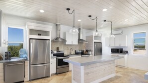 A modern kitchen with stainless steel appliances, white cabinetry, and a large island. - Compound w/Beach, Pool,  Pickleball, Gym, Kayaks, Golf Carts, Views! (Governors Harbour)