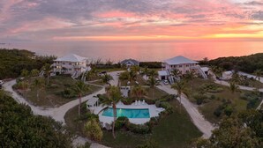 A resort with multiple buildings, a swimming pool, and a view of the ocean at sunset. - Compound w/Beach, Pool,  Pickleball, Gym, Kayaks, Golf Carts, Views! (Governors Harbour)
