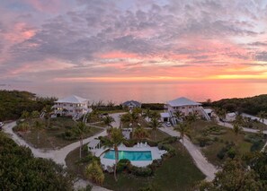 A resort with multiple buildings, a swimming pool, and a view of the ocean at sunset.