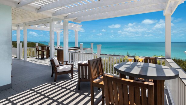 A covered outdoor area with wooden furniture and a view of the ocean. - Compound w/Beach, Pool,  Pickleball, Gym, Kayaks, Golf Carts, Views! (Governors Harbour)