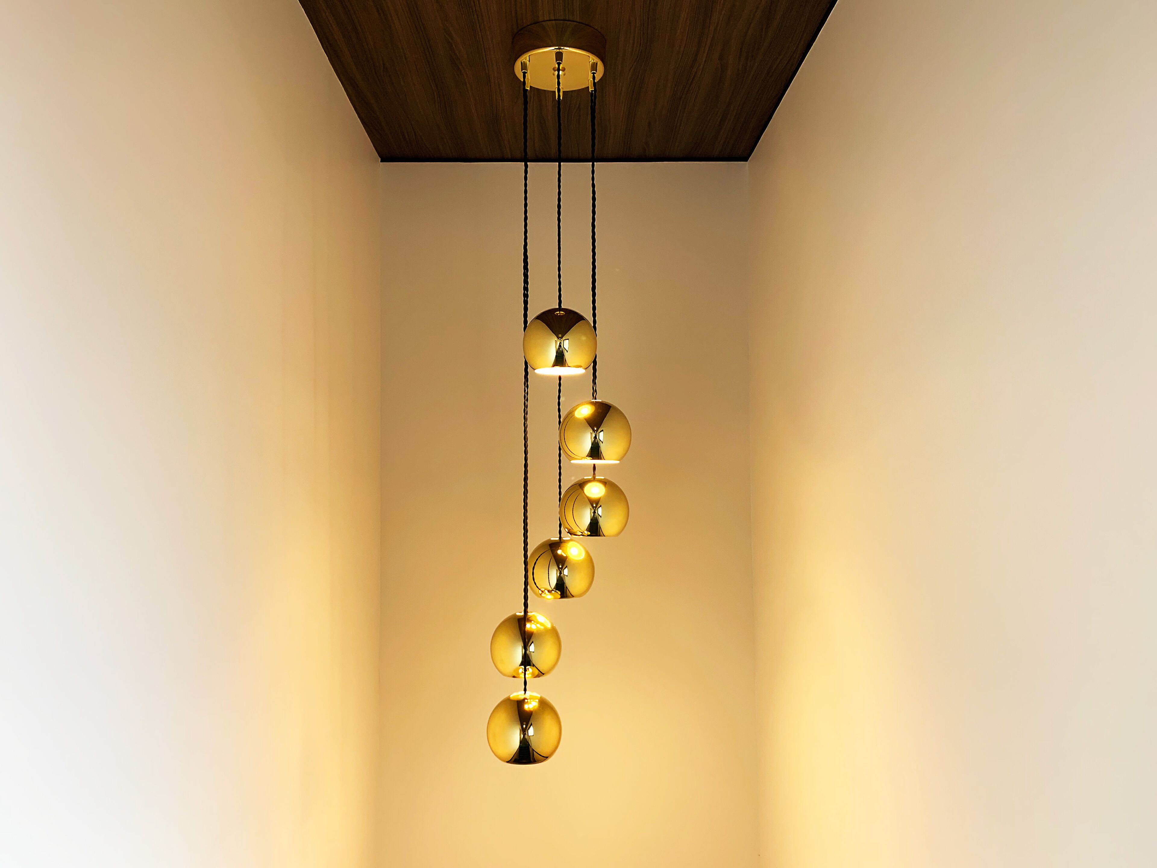 A modern chandelier with spherical light fixtures hanging from a ceiling with a wooden panel design.