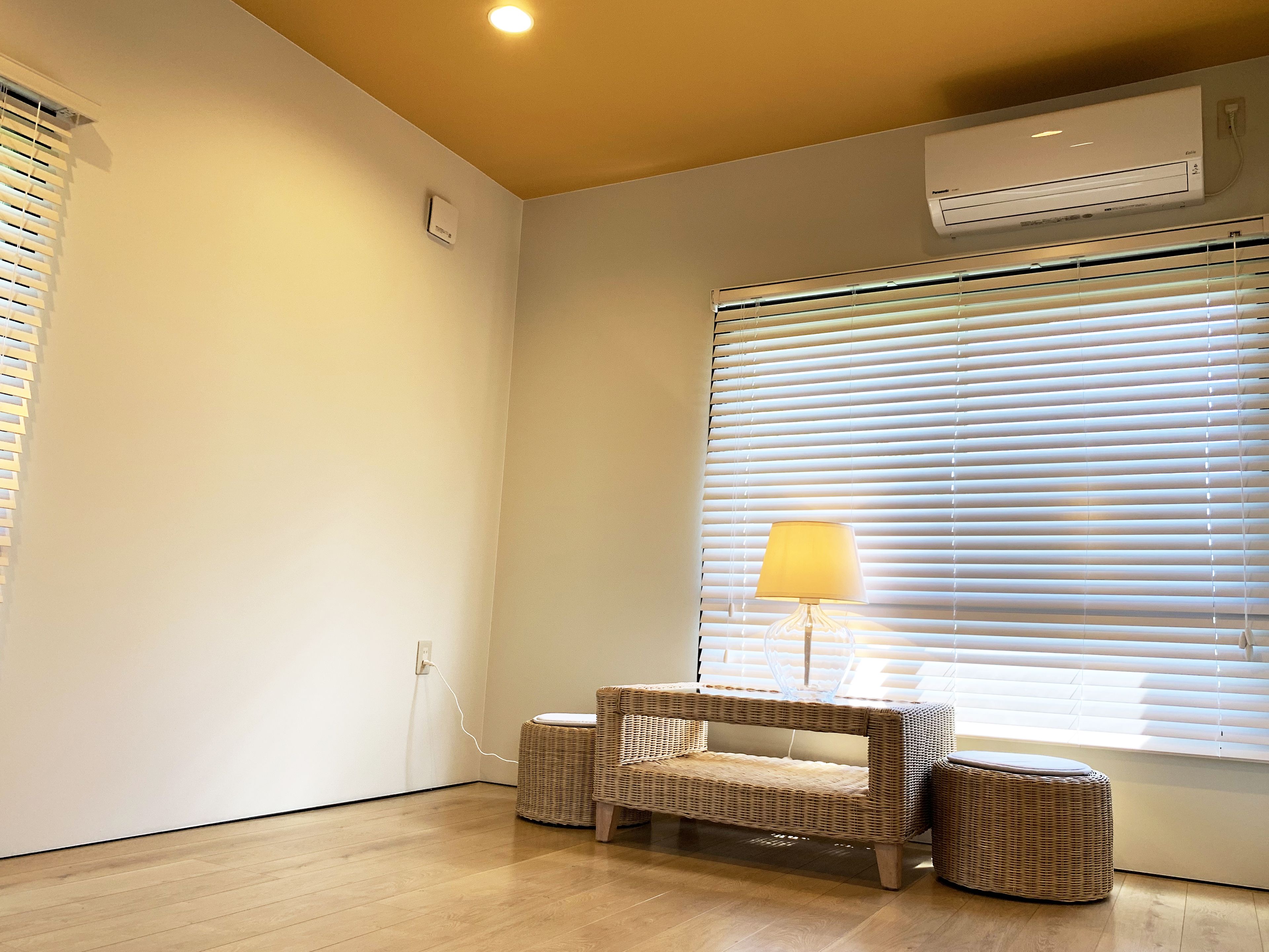 A room with a wicker sofa, a small table, and a lamp near a window with blinds.