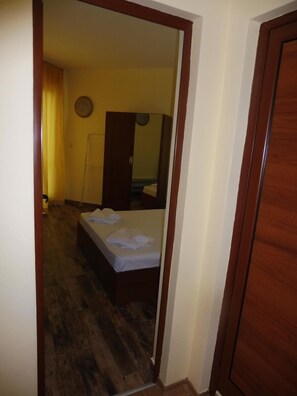 A hotel room with a wooden floor, a bed with white linens, a wooden wardrobe, and a mirror on the wall.