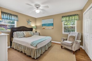 Une chambre à coucher avec un lit, une chaise, un ventilateur de plafond, une fenêtre avec des stores et un tableau au mur.