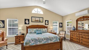 Une chambre à coucher avec un lit en bois, deux tables de chevet, une commode, une chaise et une fenêtre avec des stores.