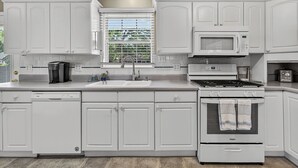 Une cuisine moderne avec des meubles blancs, un four à micro-ondes encastré, une cuisinière et un lave-vaisselle.