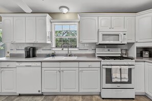 Une cuisine moderne avec des meubles blancs, un four à micro-ondes encastré, une cuisinière et un lave-vaisselle.