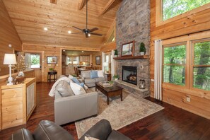 A spacious living area with a fireplace, wooden ceiling, and large windows.